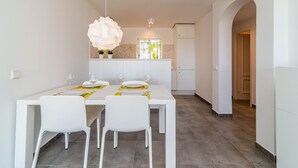 A dining area with a white table, chairs, and a large flower-shaped light fixture. - 2-Bed Apartment in Miraflores with Pool, Terrace, Garden & Wi-Fi (Mijas)