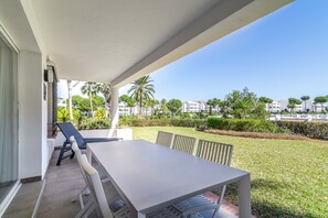 Un espace extérieur abrité, doté d’une table et de chaises, offrant une vue sur une pelouse bien entretenue et sur des bâtiments en arrière-plan.