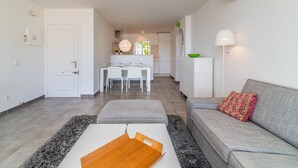 A modern living room with a grey sofa, a wooden coffee table, and a dining area with a white table and chairs. - 2-Bed Apartment in Miraflores with Pool, Terrace, Garden & Wi-Fi (Mijas)
