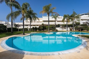 Una piscina con acqua cristallina, circondata da palme e un edificio sullo sfondo con numerosi balconi.