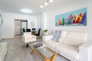 Een moderne woonkamer met een witte bank, een glazen salontafel en een schilderij van kleurrijke kristallen aan de muur.