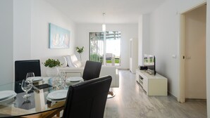 Ein modernes Wohnzimmer mit einem Glastisch, weißen Sofas, einem Flachbildfernseher und einem großen Fenster mit Blick.