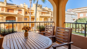 A balcony with a wooden table and chairs, a vase with flowers, and a view of multi-story buildings with balconies. - Apartment "El Albero" with Pool, Terrace & Wi-Fi (La Mata Torrevieja Alicante)