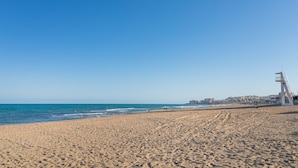 A wide sandy beach with a lifeguard tower, clear blue sky, and calm sea. - Apartment "El Albero" with Pool, Terrace & Wi-Fi (La Mata Torrevieja Alicante)