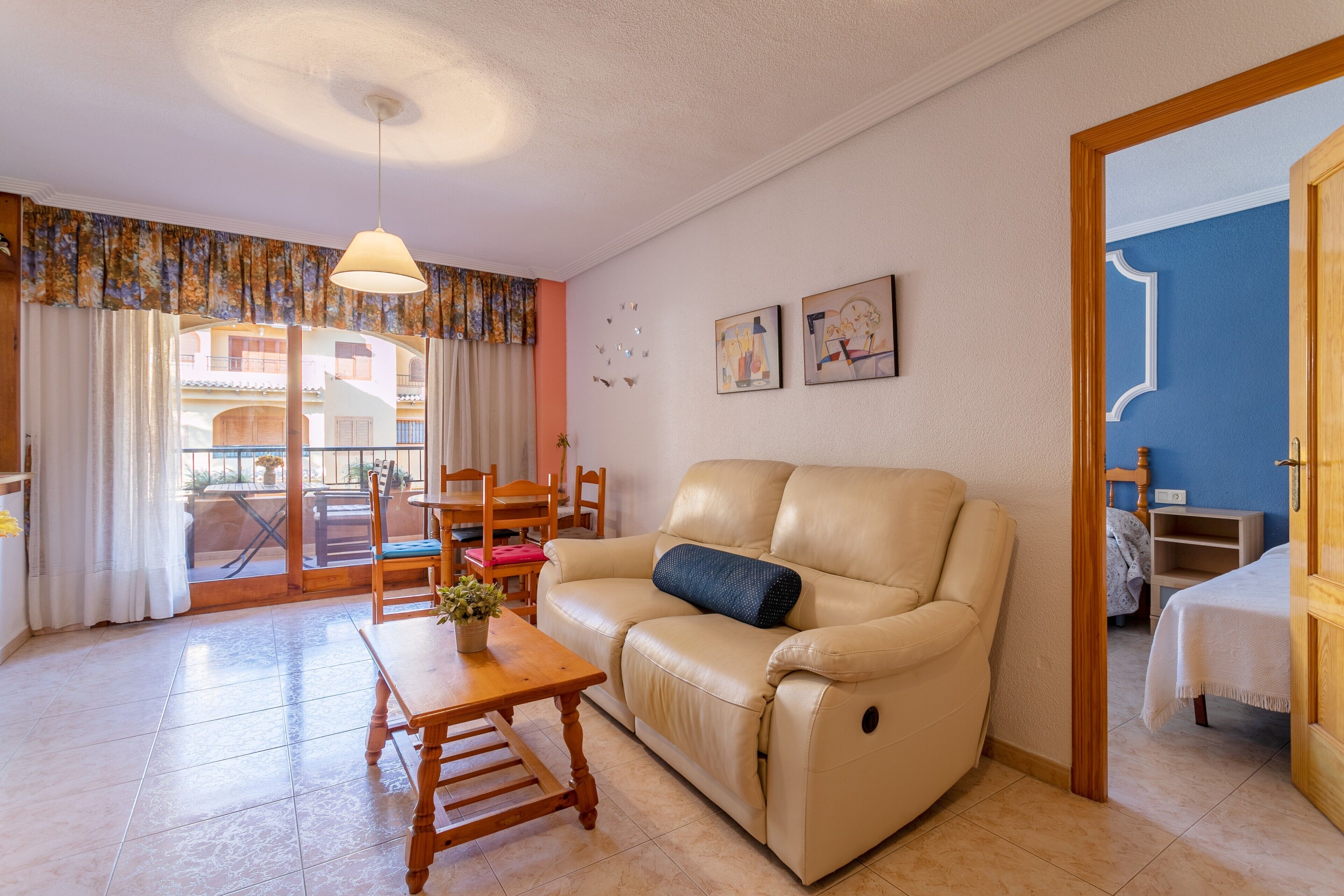 Un salon comprenant un canapé, une table en bois, un luminaire au plafond et une vue sur un espace extérieur, accessible par une porte vitrée.