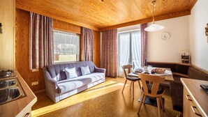 Ein gemütliches Zimmer mit Holzboden, einer Couch, einem Esstisch mit Stühlen und einer Küchenzeile.