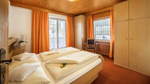Ein Hotelzimmer mit Holzboden, einem Bett mit weißen Laken, einem Schreibtisch, einem Stuhl und einem Kleiderschrank.