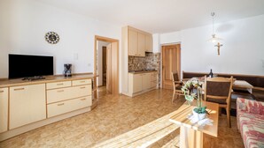 A modern kitchen with a flat-screen TV, a coffee maker, and a dining area with a table and chairs. - Apartment 'Residence Pichler 2' with Mountain View, Balcony & Wi-Fi (San Leonardo In Passiria)