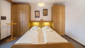 Una habitación con una cama, un armario de madera, un perchero y dos cuadros en la pared.