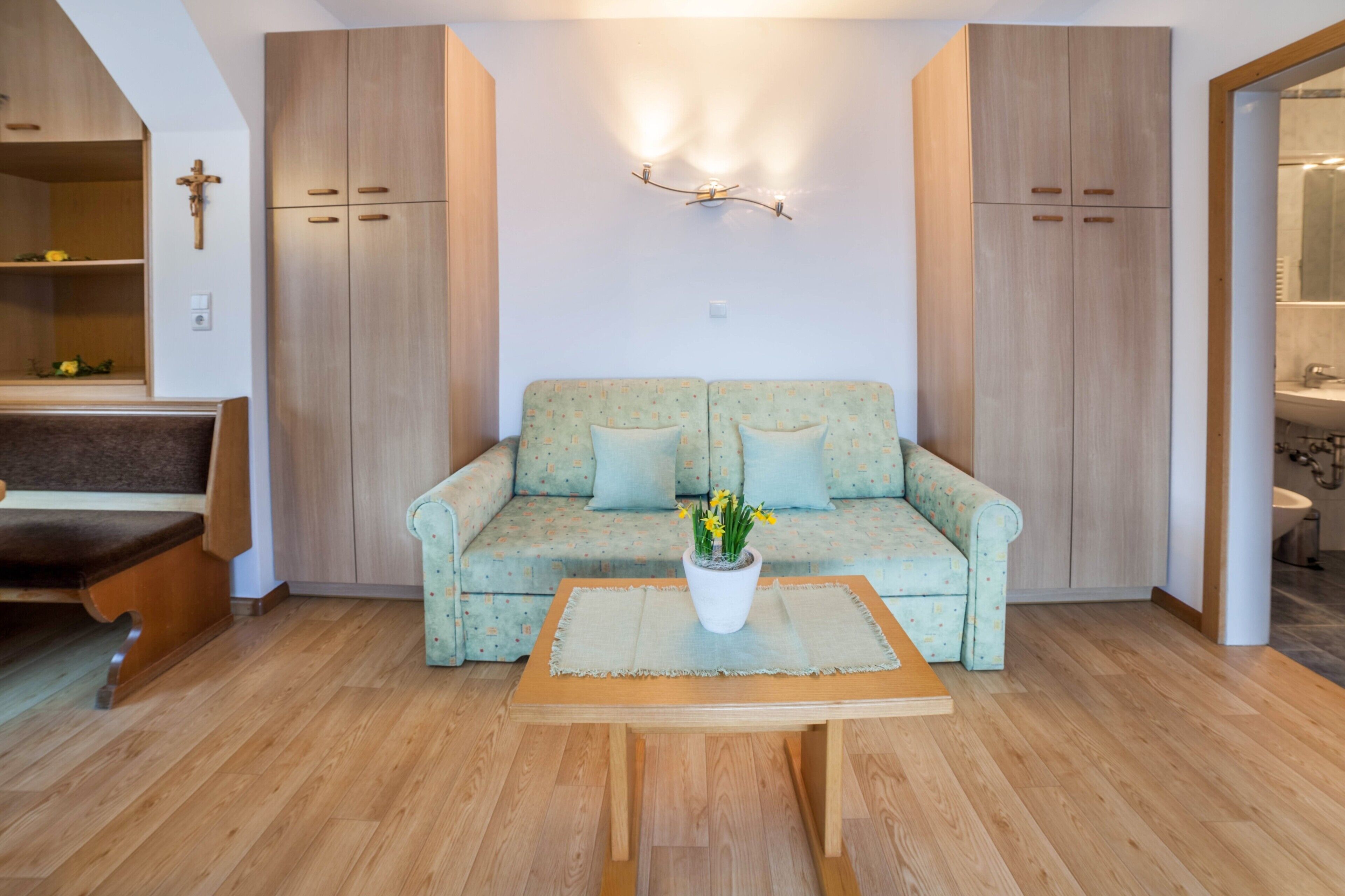 Een woonkamer met een bank, een bijzettafeltje, houten kasten en een wandlamp.