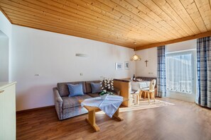 A living room with a wooden ceiling, a sofa, a coffee table, a dining area, and a large window with curtains.
