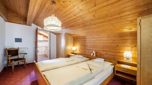 Ein Zimmer mit Holzwänden, einem Bett, Nachttischlampen, einem Sessel und einem Heizkörper.
