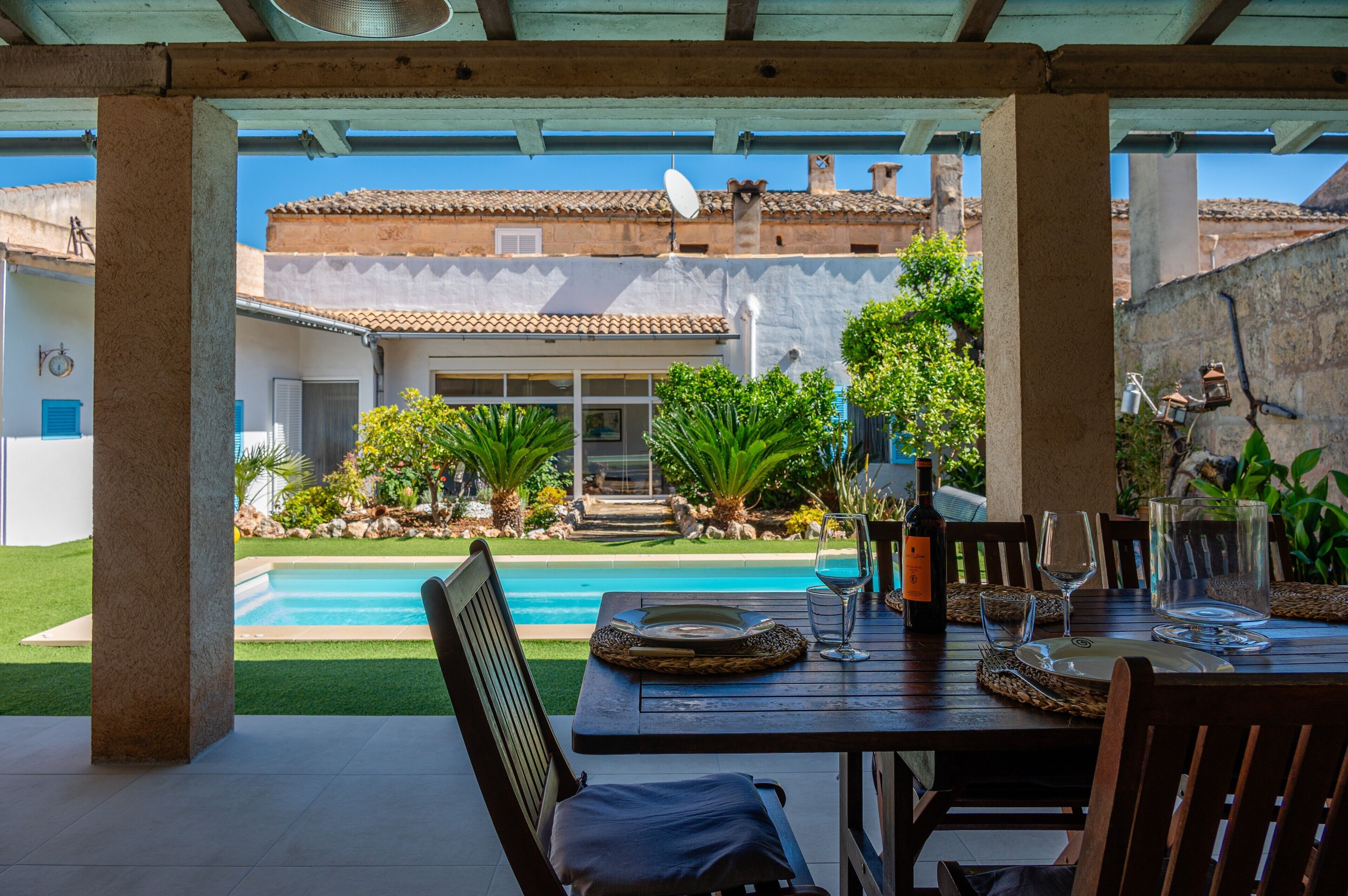 Un patio techado con piscina, mesa de comedor, sillas y vistas a un edificio con tejado de tejas.