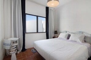 A bedroom with a bed, a window, curtains, a bedside lamp, and a small table with a tray.