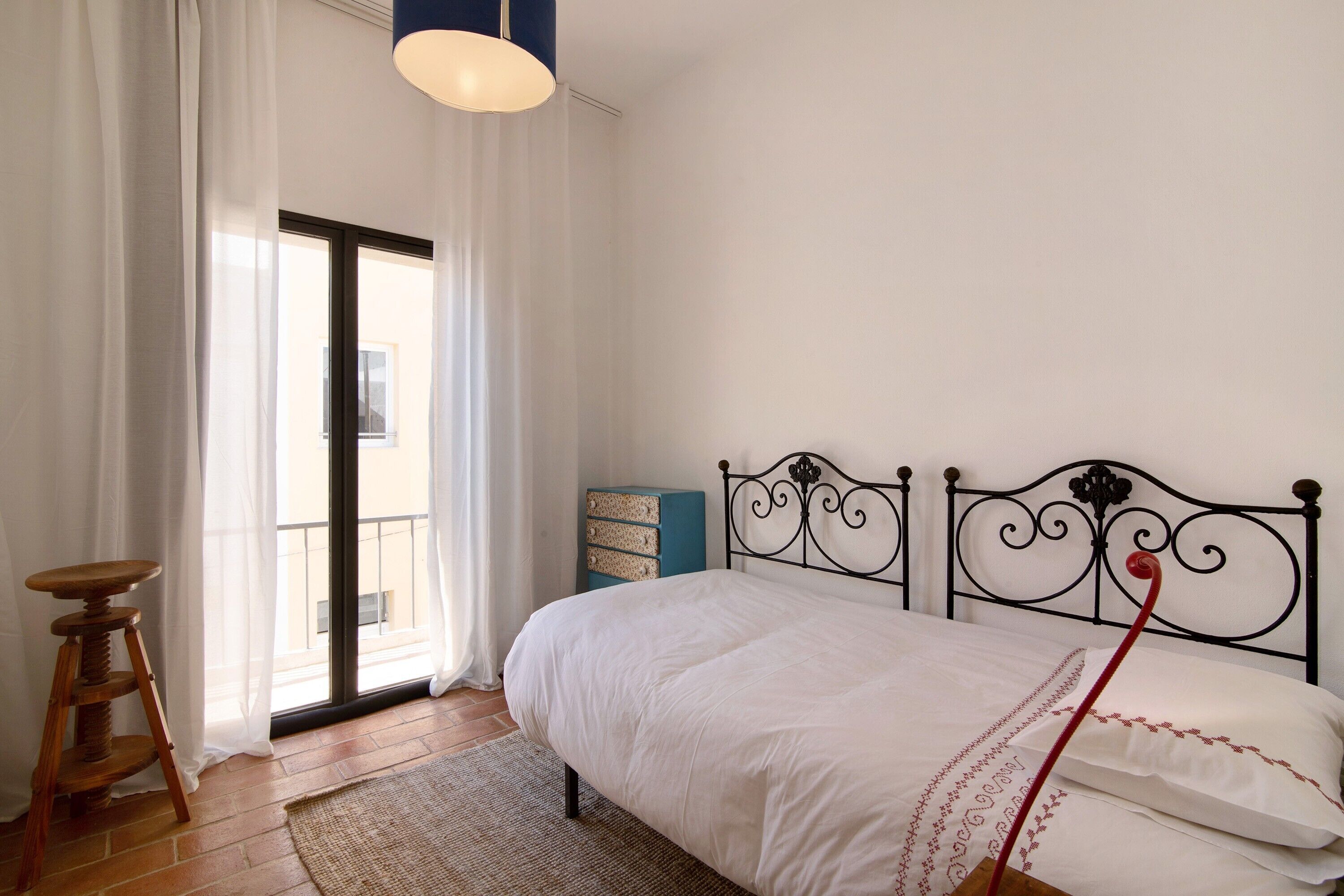 A bedroom with a bed, a wooden side table, a blue cabinet, and a balcony door.
