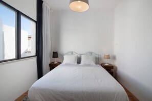 Une chambre à coucher avec un lit, deux tables de chevet, une fenêtre et un luminaire au plafond.
