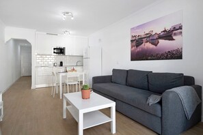 Un salon moderne avec un canapé gris, une table basse blanche et un coin repas comprenant une table et des chaises blanches.
