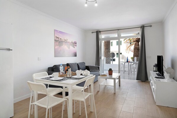 Un espace de vie moderne comprenant un coin repas, un canapé, un téléviseur et une vue sur l’extérieur grâce à une porte vitrée.