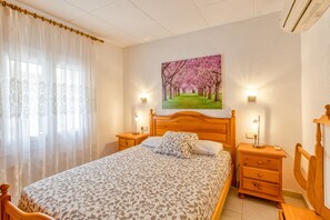 Een slaapkamer met een groot bed, twee nachtkastjes, een houten hoofdbord, een aan de muur hangend schilderij en een raam met dunne gordijnen.