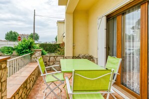 Een balkon met een tafel en stoelen, een stenen muur en uitzicht op de straat.