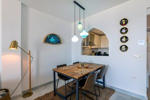 Un espace repas comprenant une table en bois, des chaises, des luminaires suspendus, une lampe sur pied et des horloges murales.