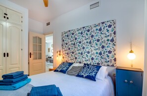 Une chambre à coucher comprenant un lit, une table de chevet, une lampe fixée au mur, une armoire bleue et une porte donnant sur une autre pièce.