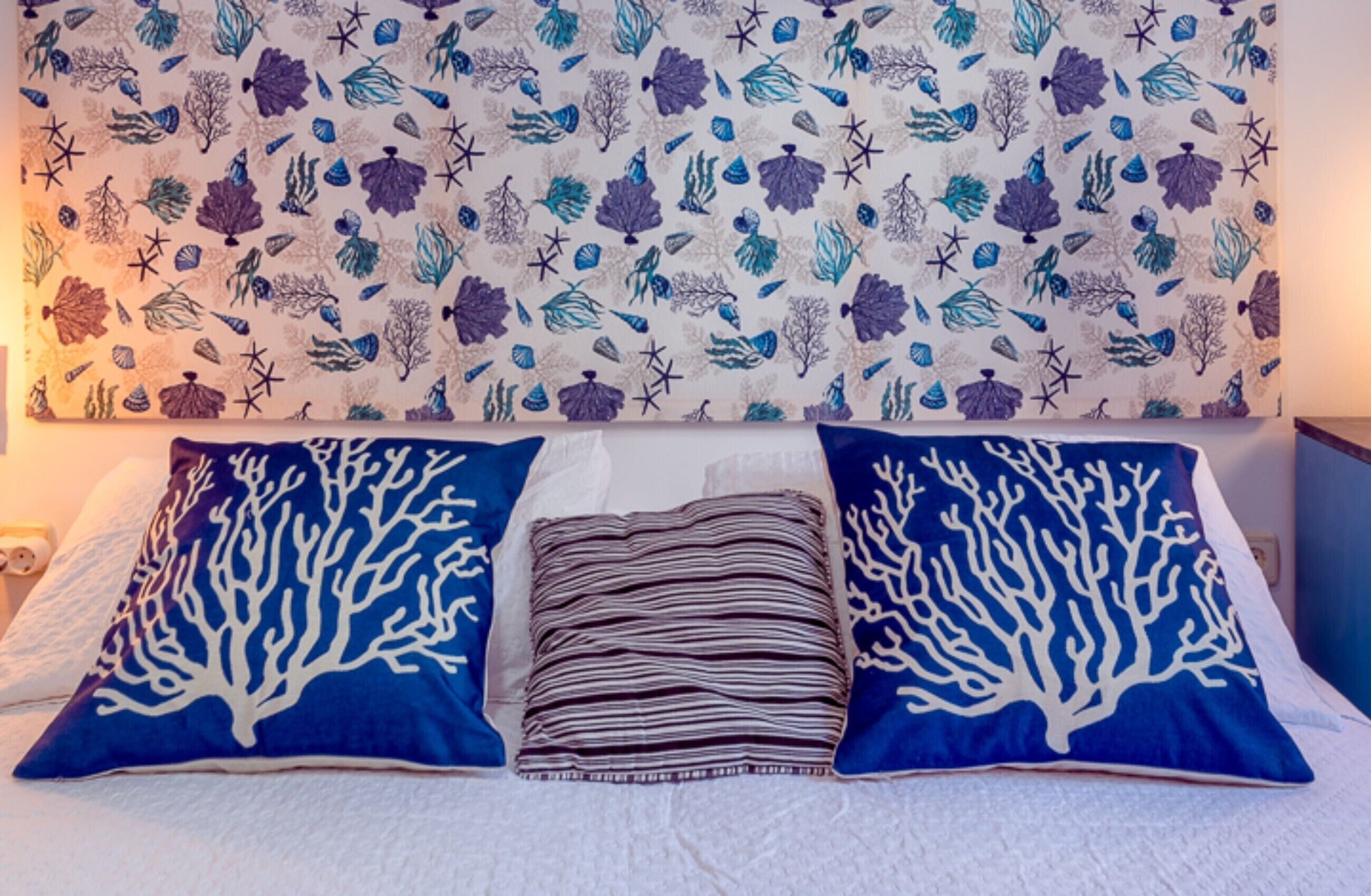 A bed with two pillows, a folded blanket, and a wall with a marine-themed pattern.