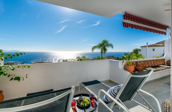 Un balcon avec une table, des chaises, un pot de fleurs et une vue sur la mer.