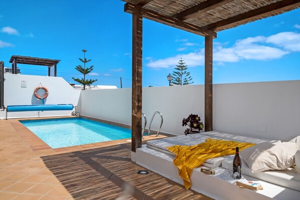 Une piscine sur le toit avec un bord bleu, un canapé d’extérieur blanc agrémenté d’un plaid jaune et une structure en forme de pergola.