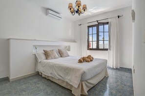 Une chambre à coucher avec un lit, des oreillers, une serviette enroulée, une fenêtre avec des rideaux et un appareil de climatisation.