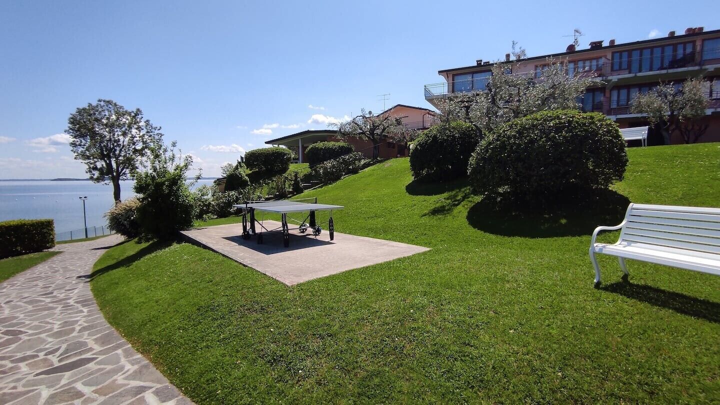 A grassy outdoor area with a table and bench, a paved walkway, and a building with balconies.
