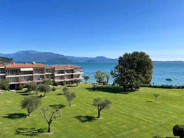 A multi-story building with balconies overlooking a lake, surrounded by well-maintained grass and trees.
