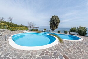 Una piscina con pavimento in pietra, circondata dal verde e vista mare.