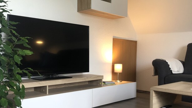 Ett modernt vardagsrum med en platt-TV, en träinredd mediabänk, en svart soffa och ett litet bord.