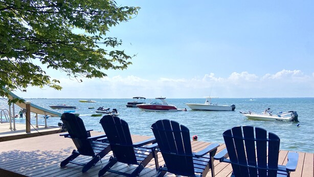 Une terrasse en bois avec quatre chaises Adirondack donnant sur une marina où sont amarrés plusieurs bateaux.