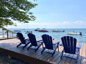 Een houten terras met vier Adirondack-stoelen, gericht op een jachthaven met verschillende boten.