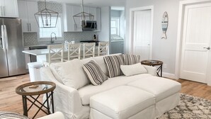 Un salon moderne avec un canapé d’angle blanc, un tapis moelleux et un coin repas comprenant une table et des chaises blanches.