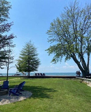 A grassy area with a view of the ocean, a wooden deck, and blue Adirondack chairs.