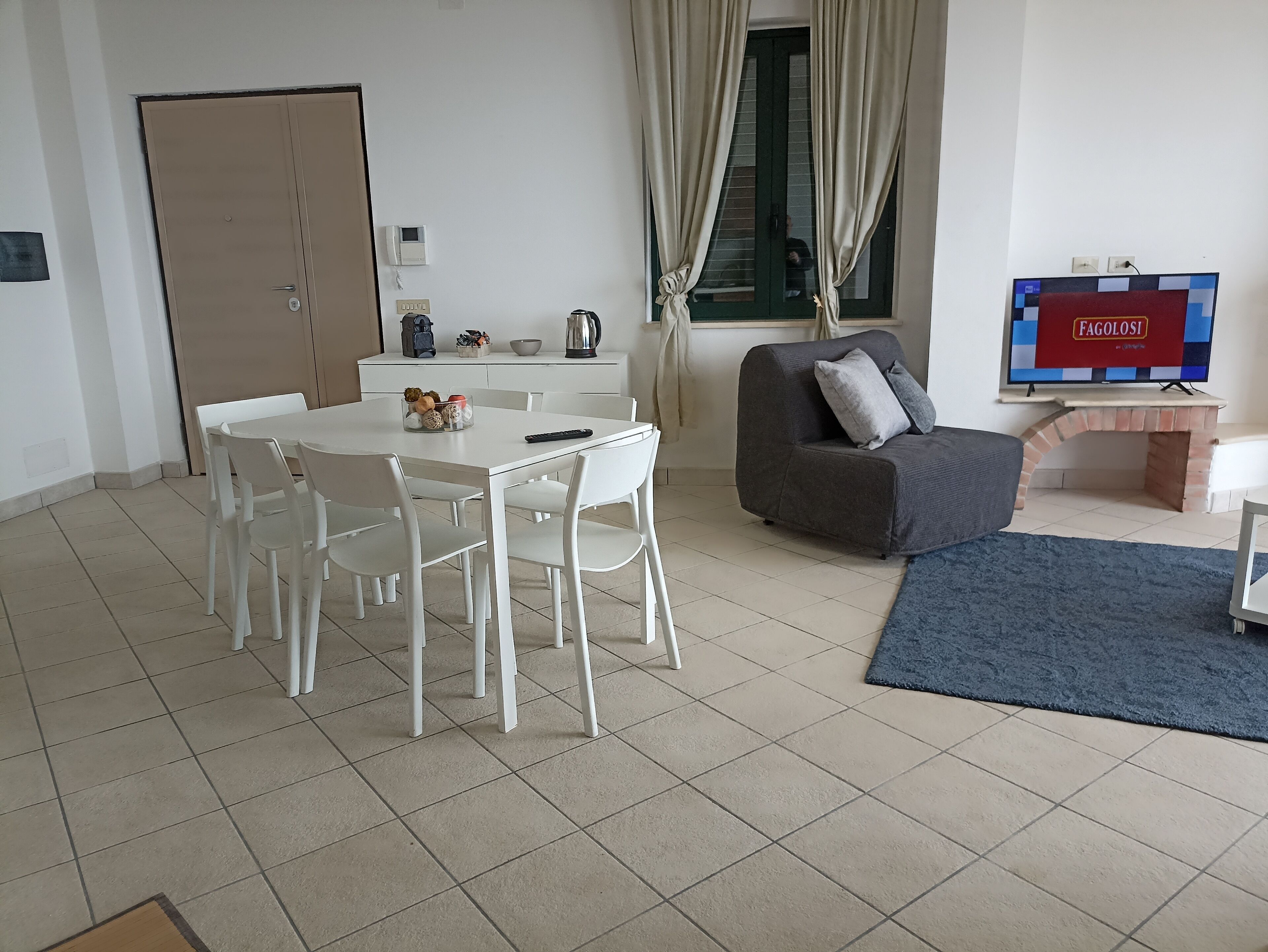 A modern living room with a dining table, white chairs, a grey sofa, a TV, and a fireplace.