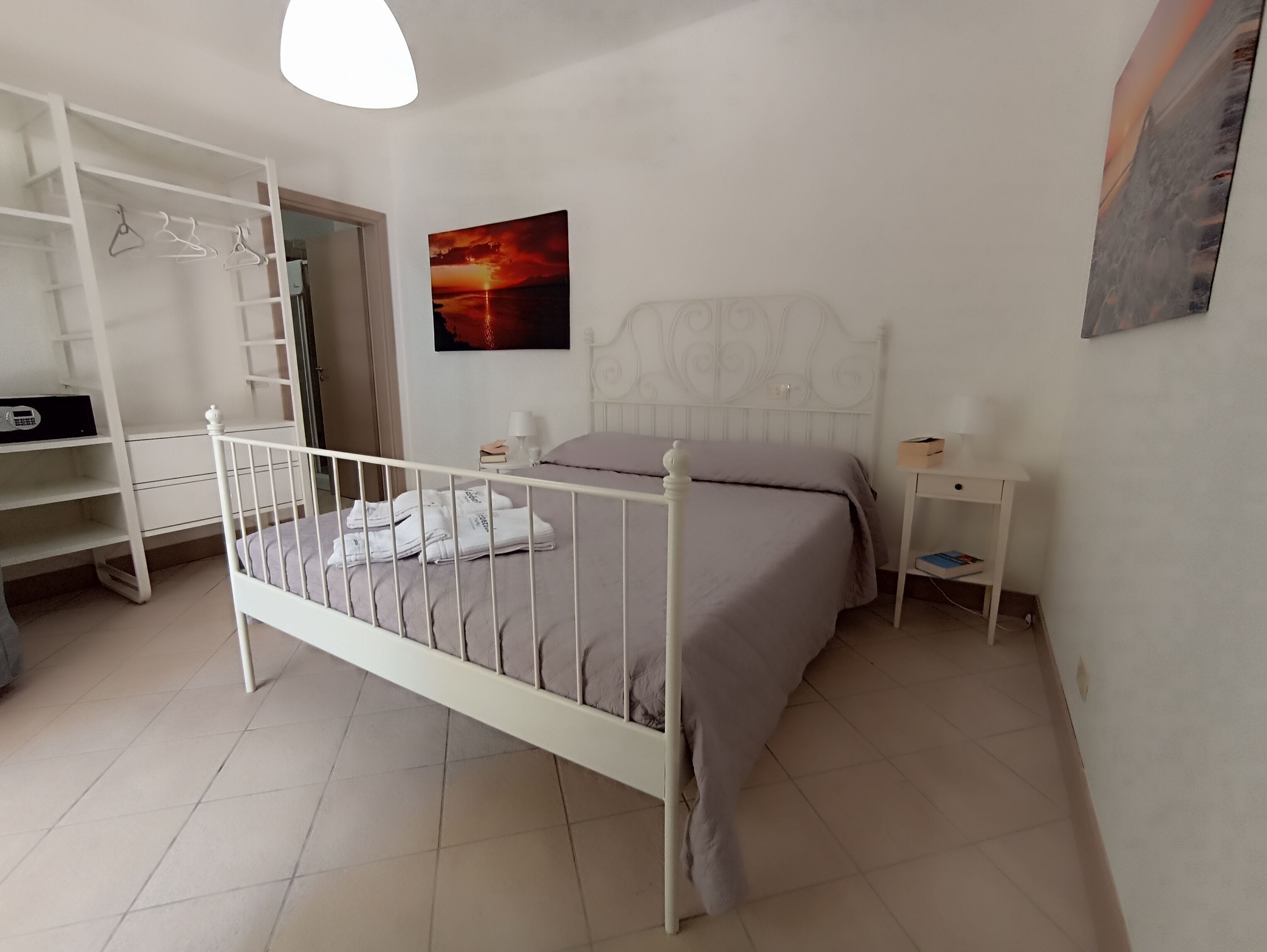 A bedroom with a bed, a wardrobe, a nightstand, and a painting on the wall.
