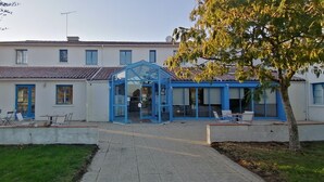 A two-story building with a blue entrance and a covered patio area. - Le Mas des Marais (Machecoul-Saint-Même)