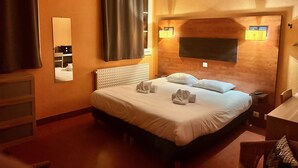 A hotel room with a large bed, a bedside table, a mirror, and a window with curtains. - Le Mas des Marais (Machecoul-Saint-Même)