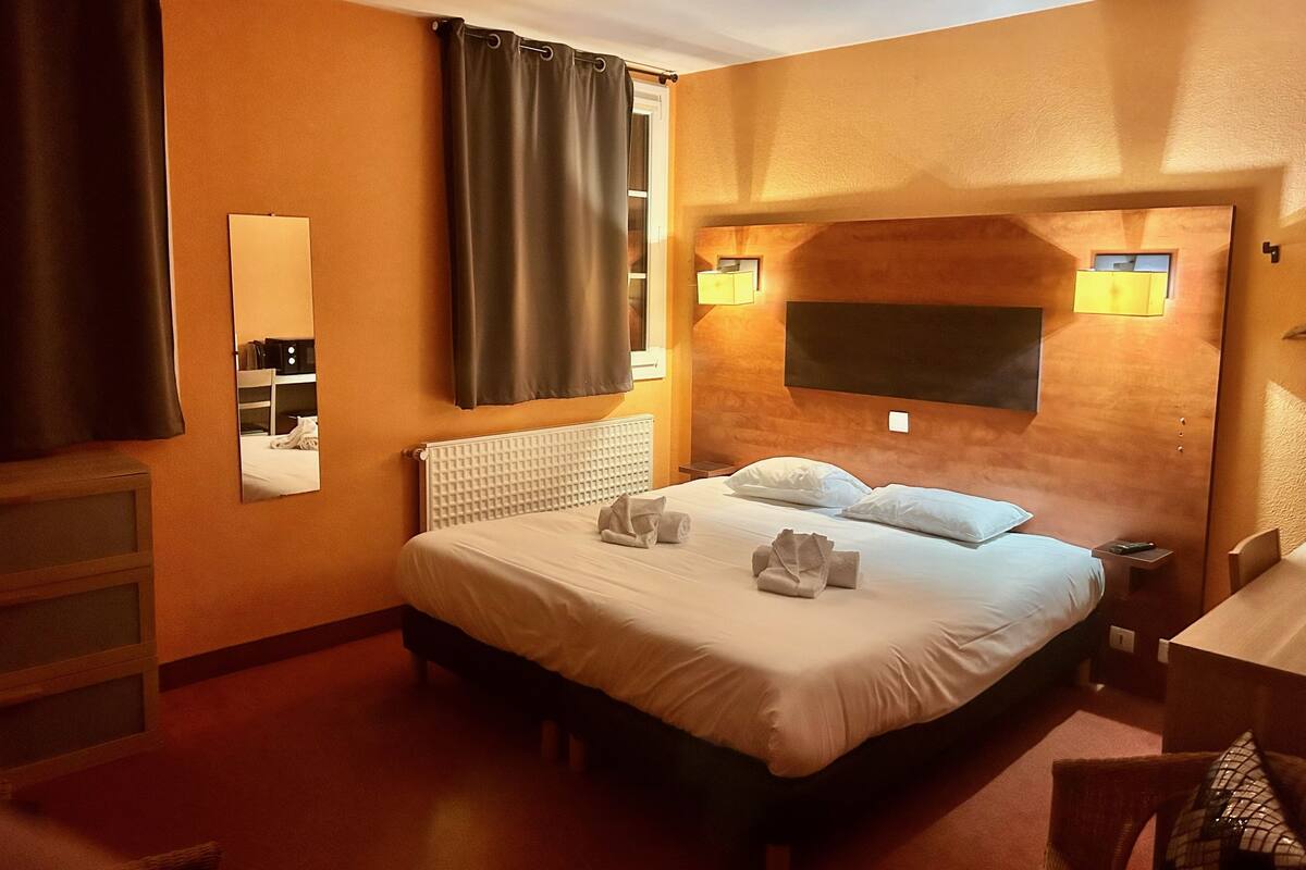 Een hotelkamer met een groot bed, een nachtkastje, een spiegel en een raam met gordijnen.
