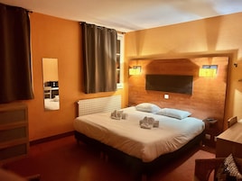 Quarto de hotel com uma cama grande, uma mesa de cabeceira, um espelho e uma janela com cortinas.