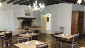 A restaurant with wooden tables and chairs, a chandelier, and a fireplace. - Le Mas des Marais (Machecoul-Saint-Même)