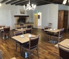 Restaurante com mesas e cadeiras de madeira, um lustre e uma lareira.