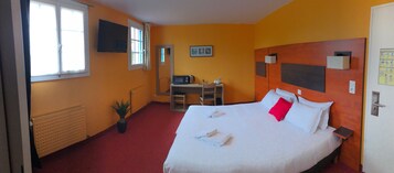 Habitación de hotel con cama, escritorio, televisor y radiador.
