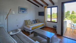 A cozy living room with a sofa, a bed, a table, and a TV on the wall.