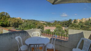 A terrace with a table and chairs, overlooking a hillside with buildings and trees.