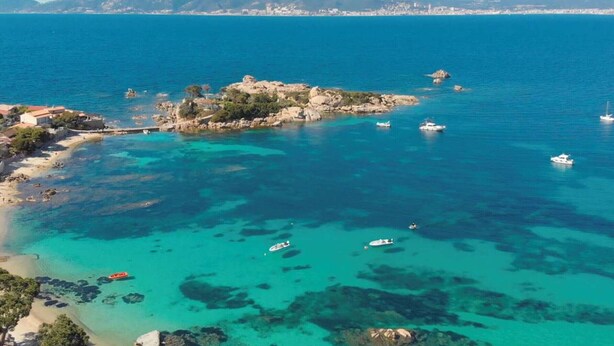 A coastal area with clear turquoise waters, a small rocky island, and boats.